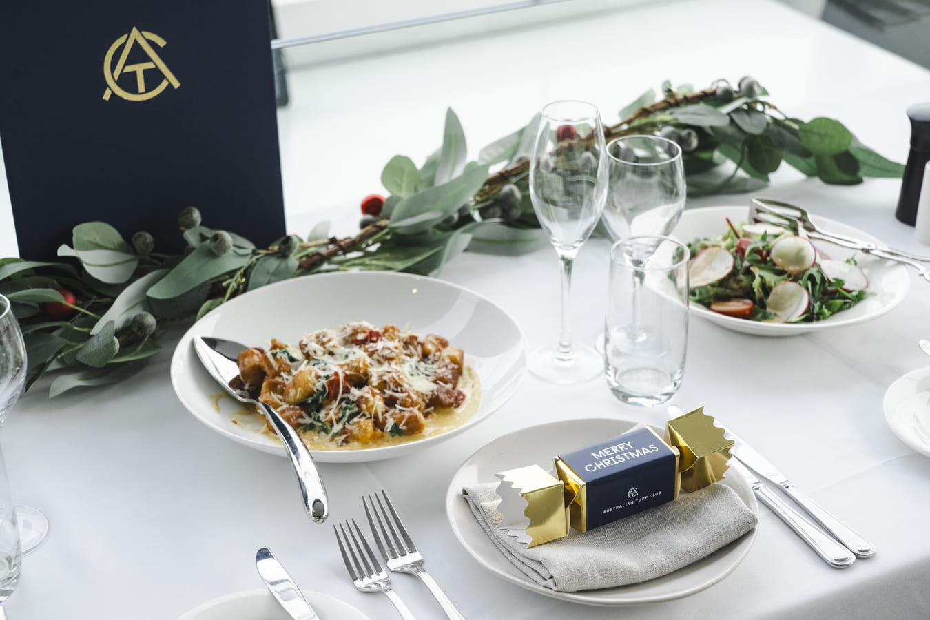 A Christmas themed table setting containing dishes, glasses and a cracker